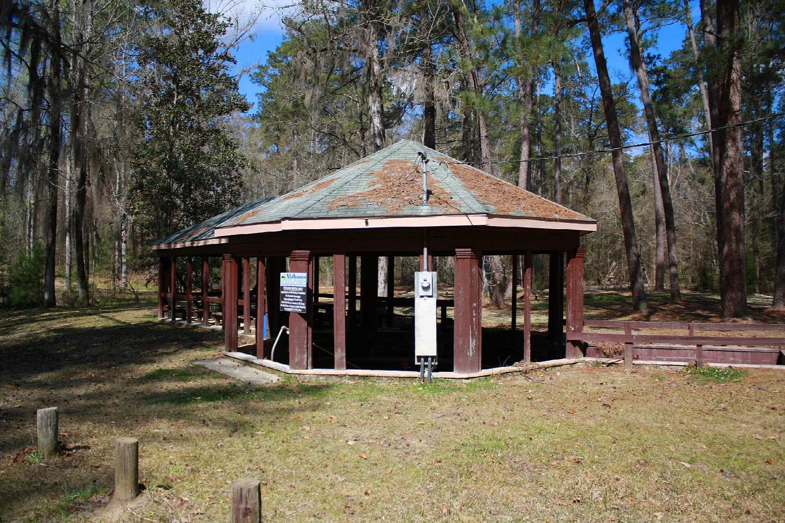 Octagonal wooden pavilion over a spring in a clearing among tall pines
