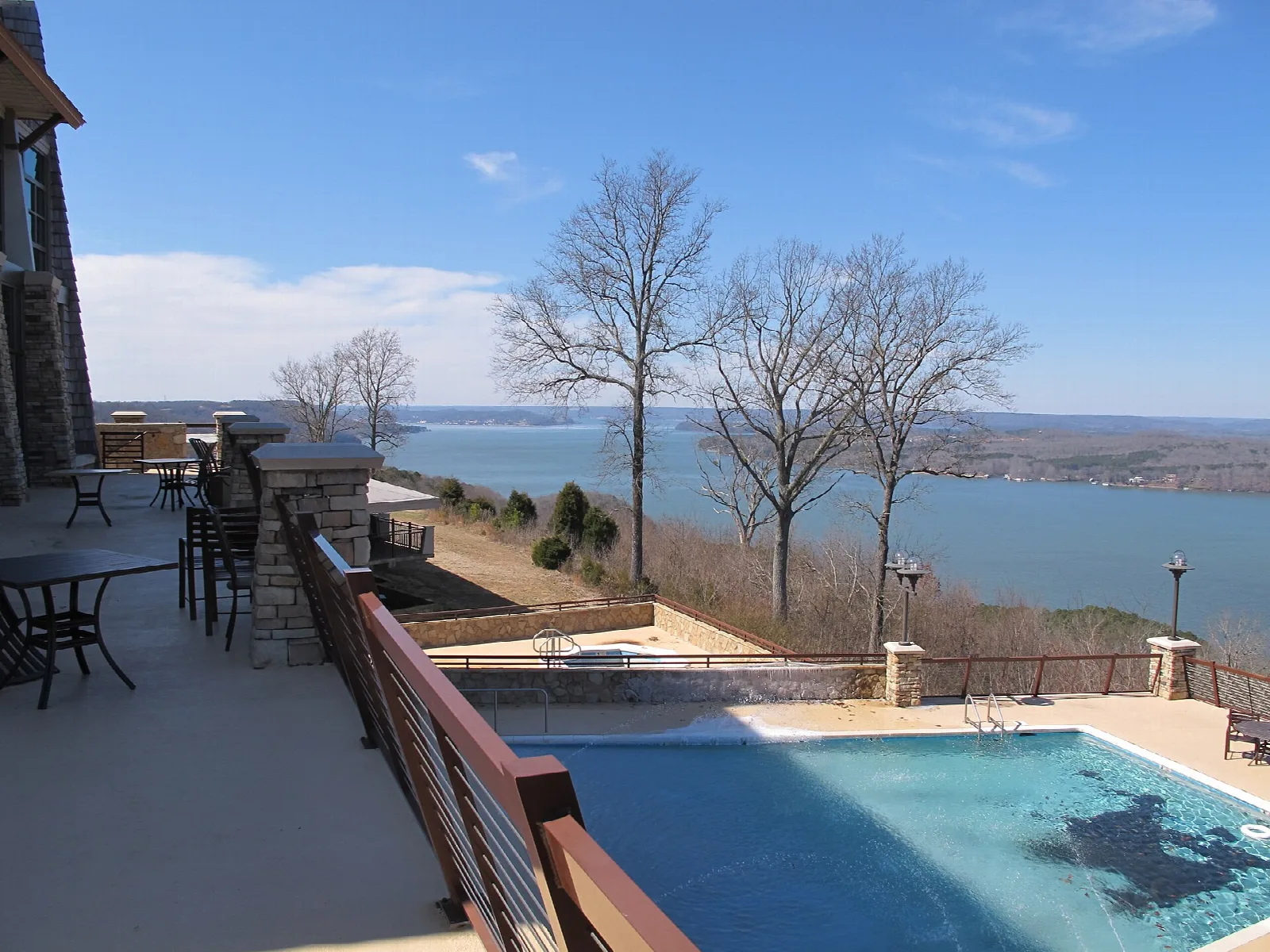 Stone terrace with a pool and railing overlooking a wide lake and far shore