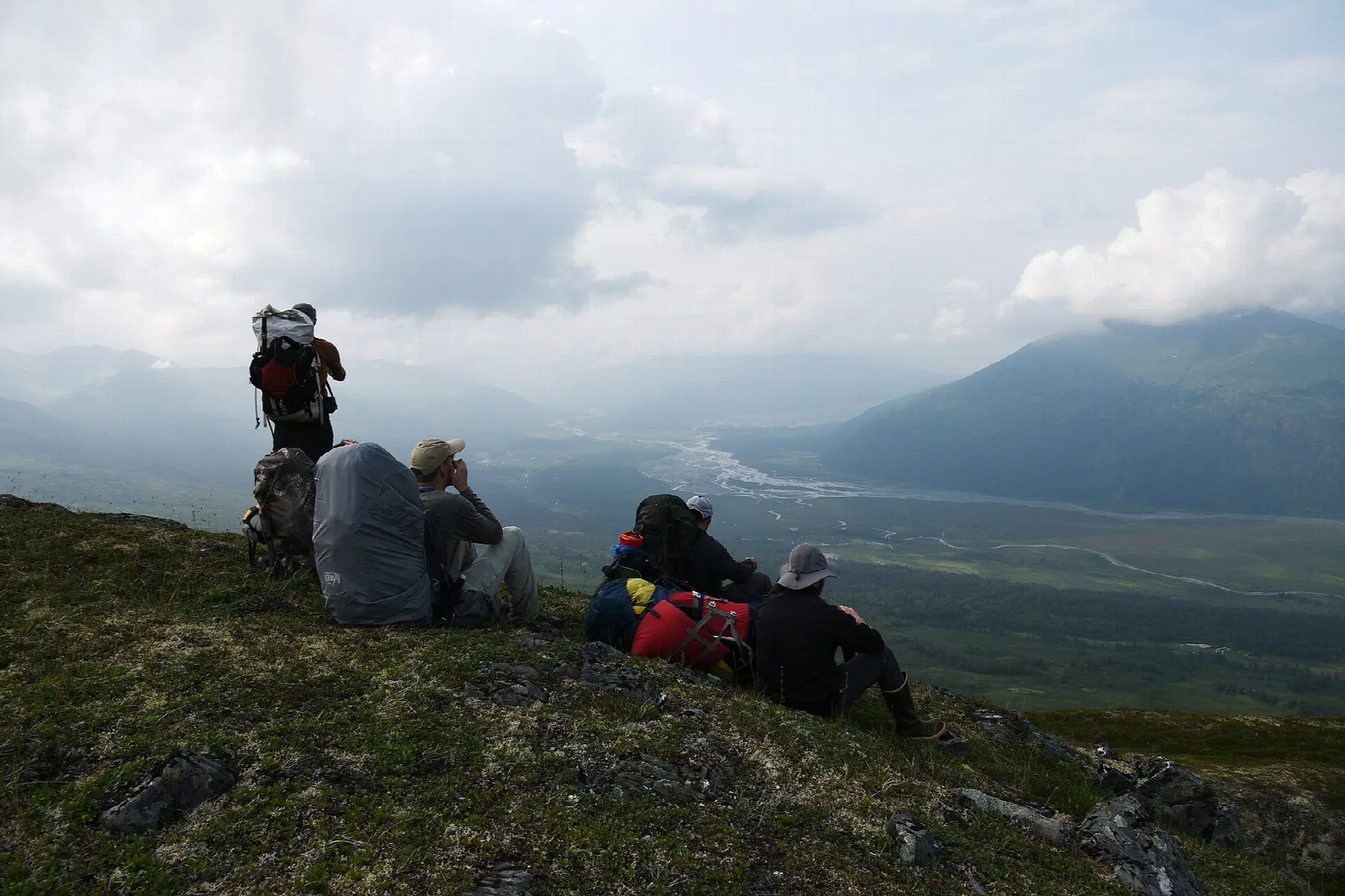 Hikers resting on a green ridge above a wide river valley