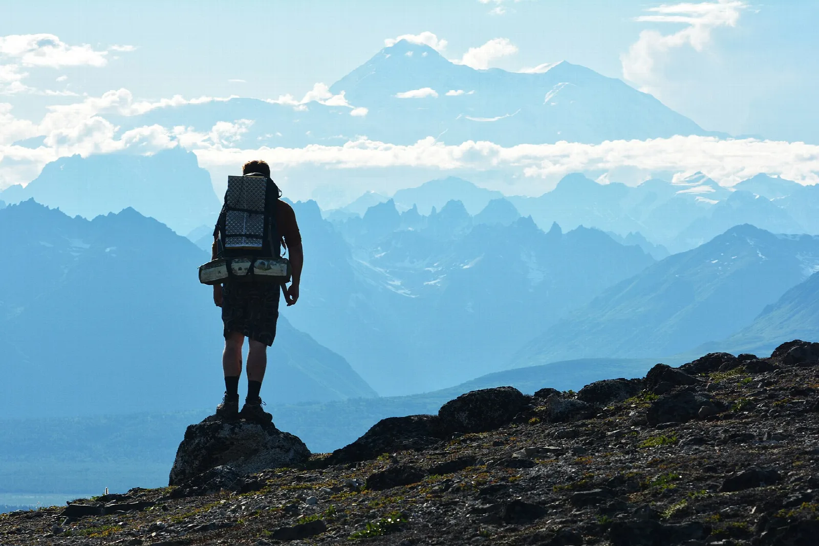 Hiker with a pack standing on a rocky ridge, looking over blue layered mountains