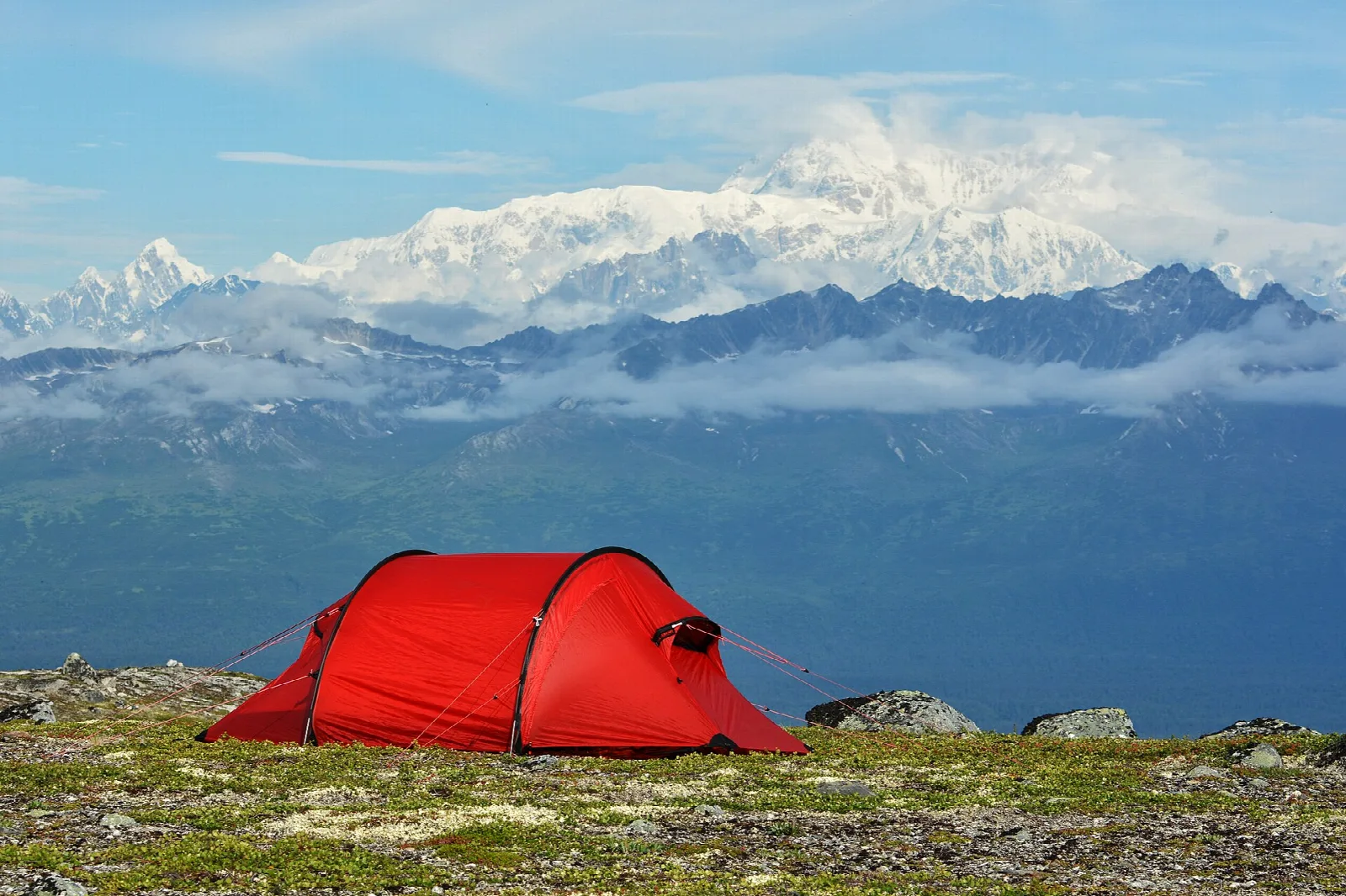 Red tent on a tundra ridge with a snow-covered mountain range behind