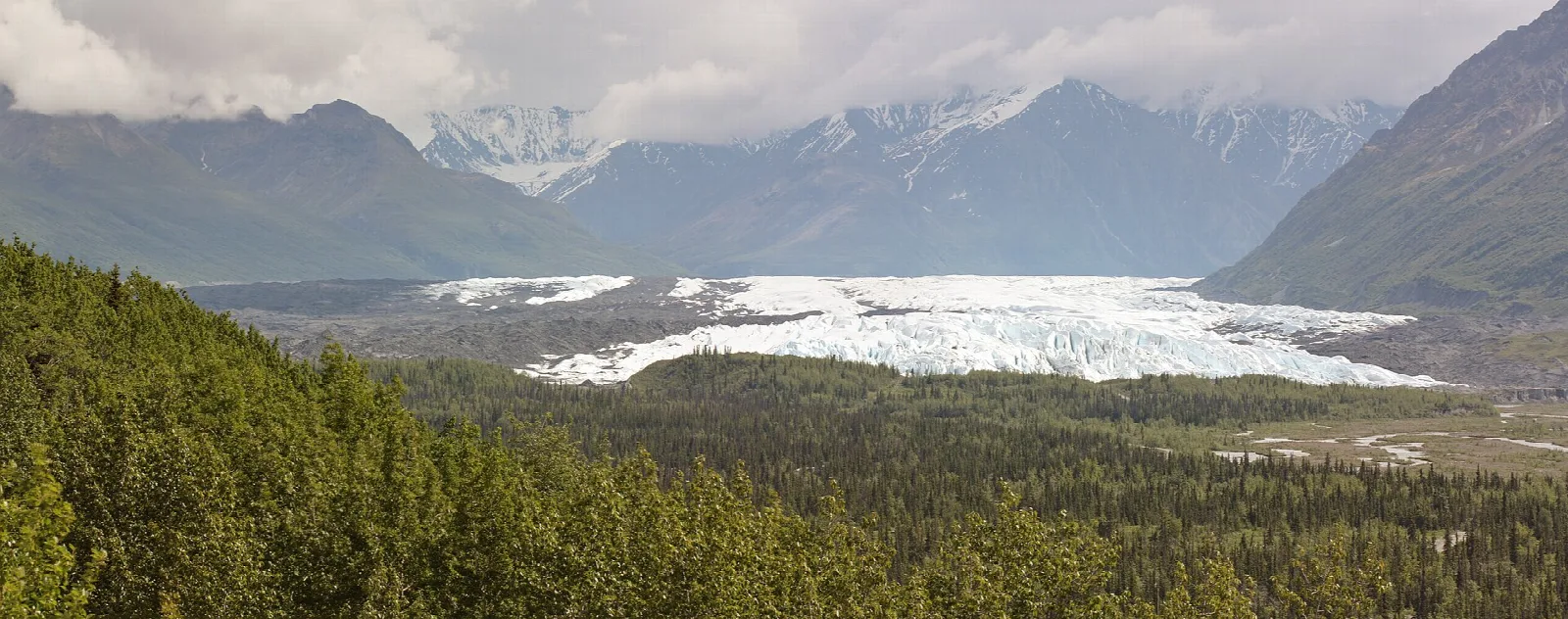Wide panorama of the glacier and valley beneath cloudy mountains