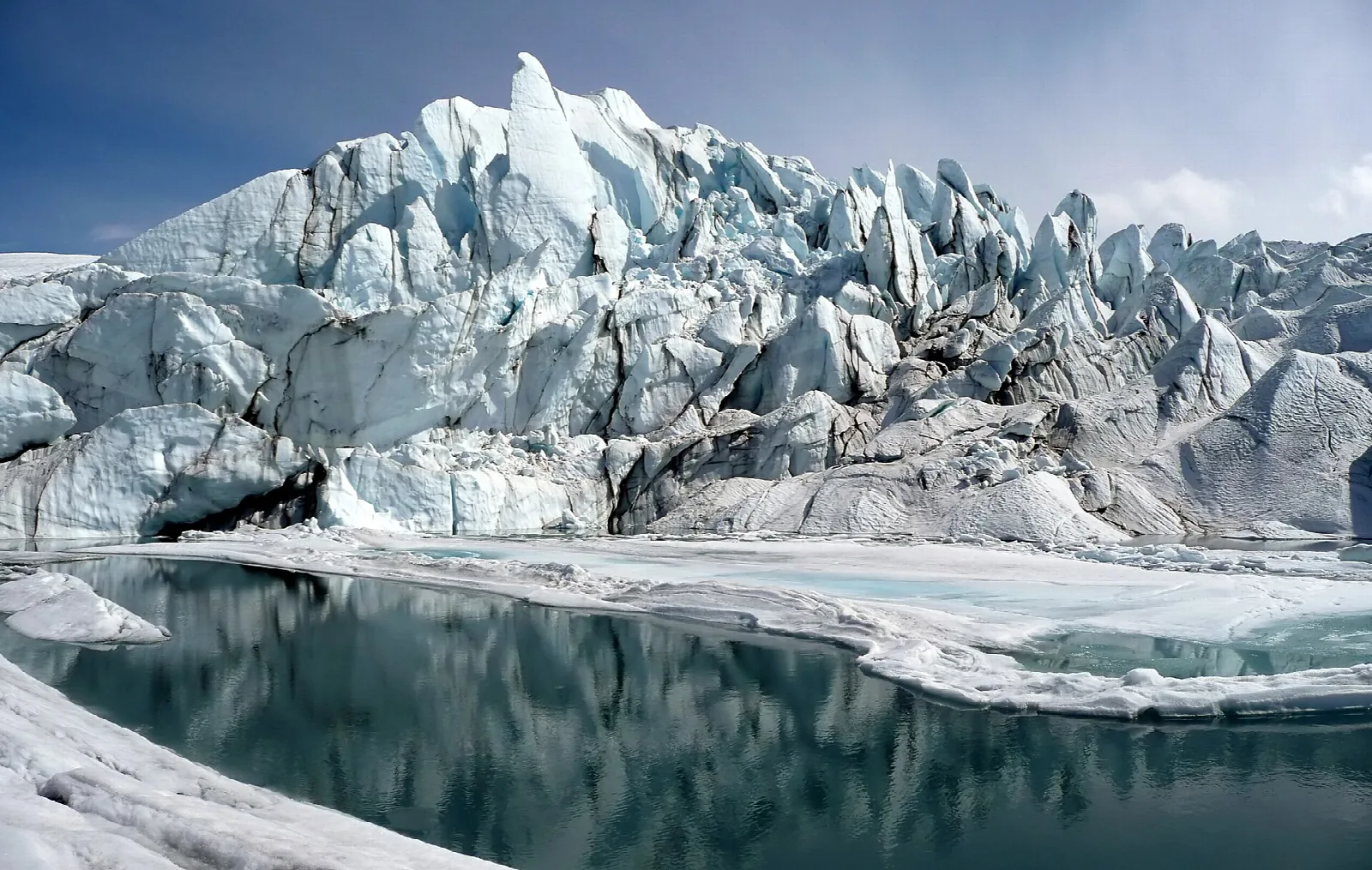 Tall jagged ice at the glacier's end, beside a dark meltwater pool