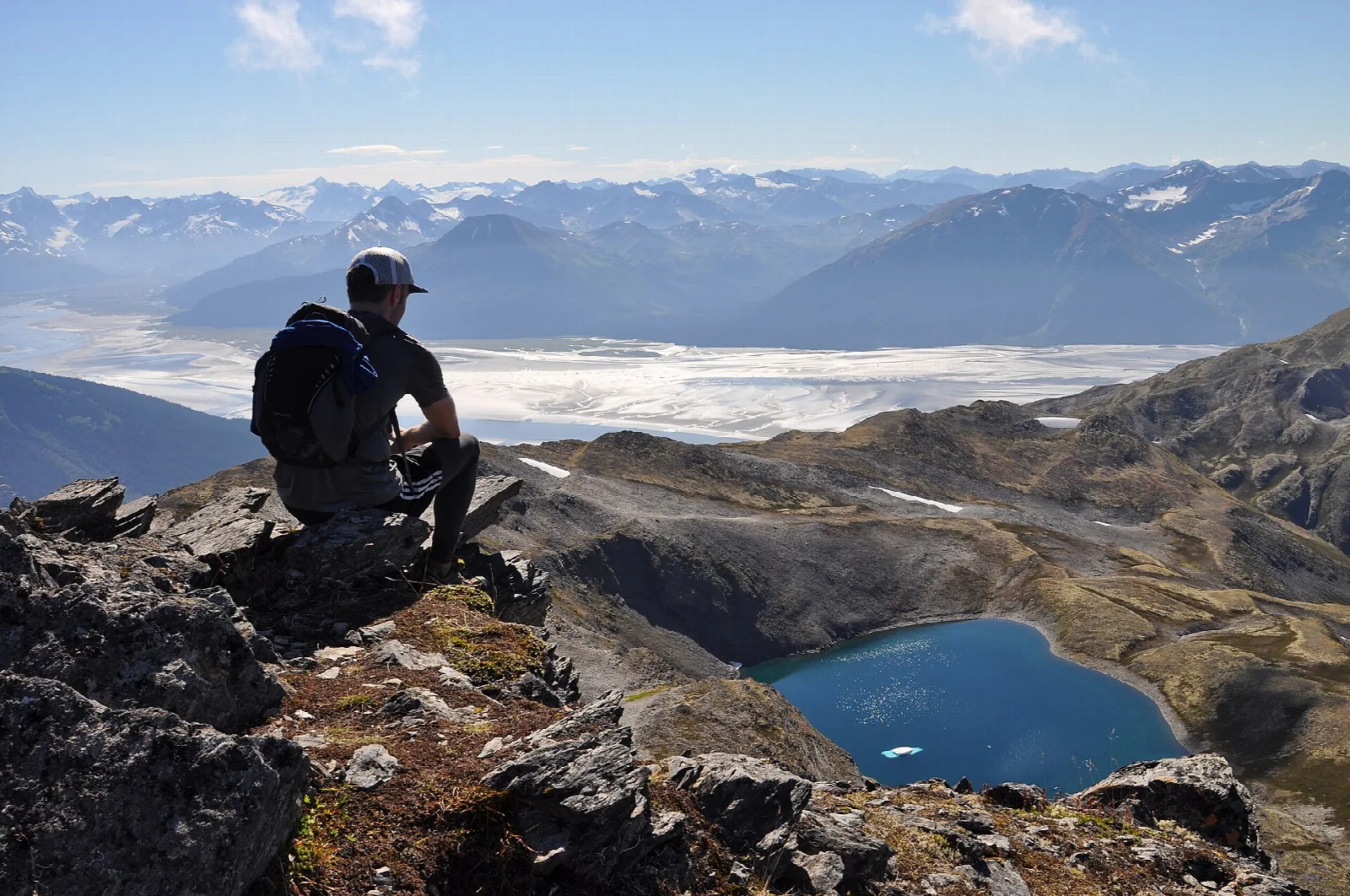 Hiker sitting on a rock above a blue alpine lake and wide mountain valley