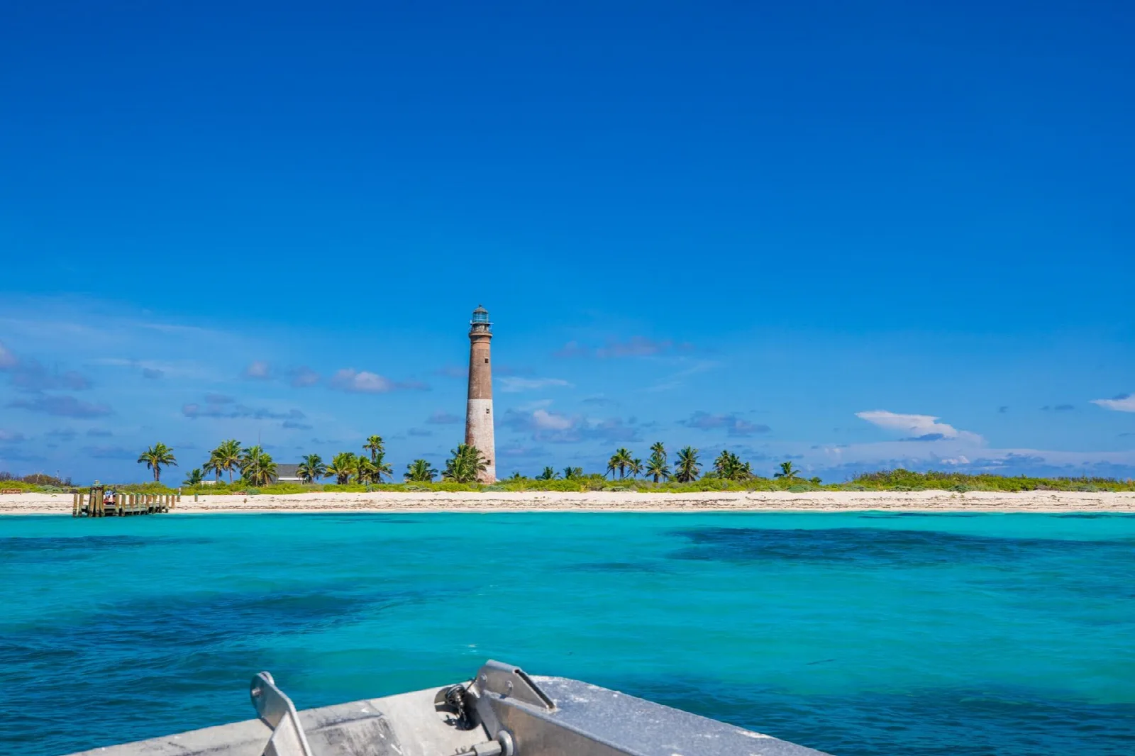 A tall lighthouse on a low palm-fringed island across bright turquoise water