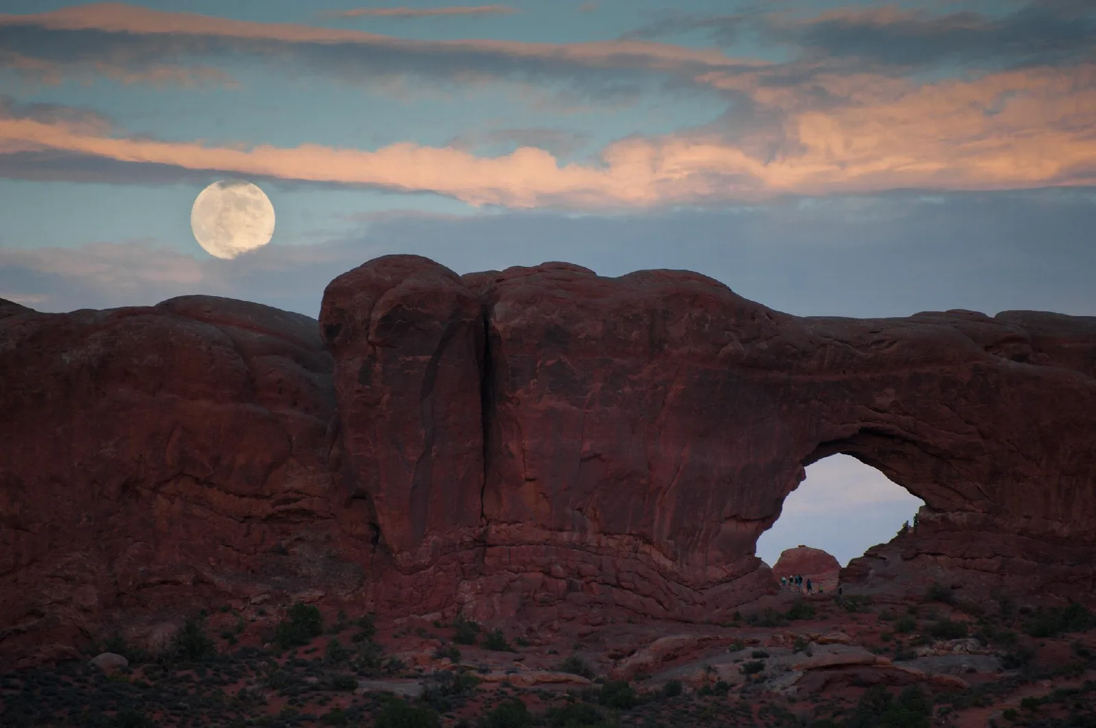 Large sandstone arch at dusk with a large white moon and clouds above
