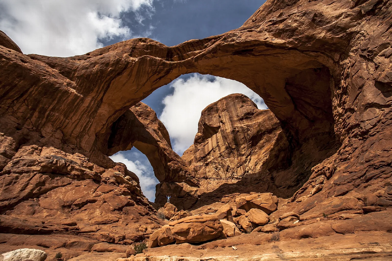 Two massive sandstone arches springing from the same base under a partly cloudy sky