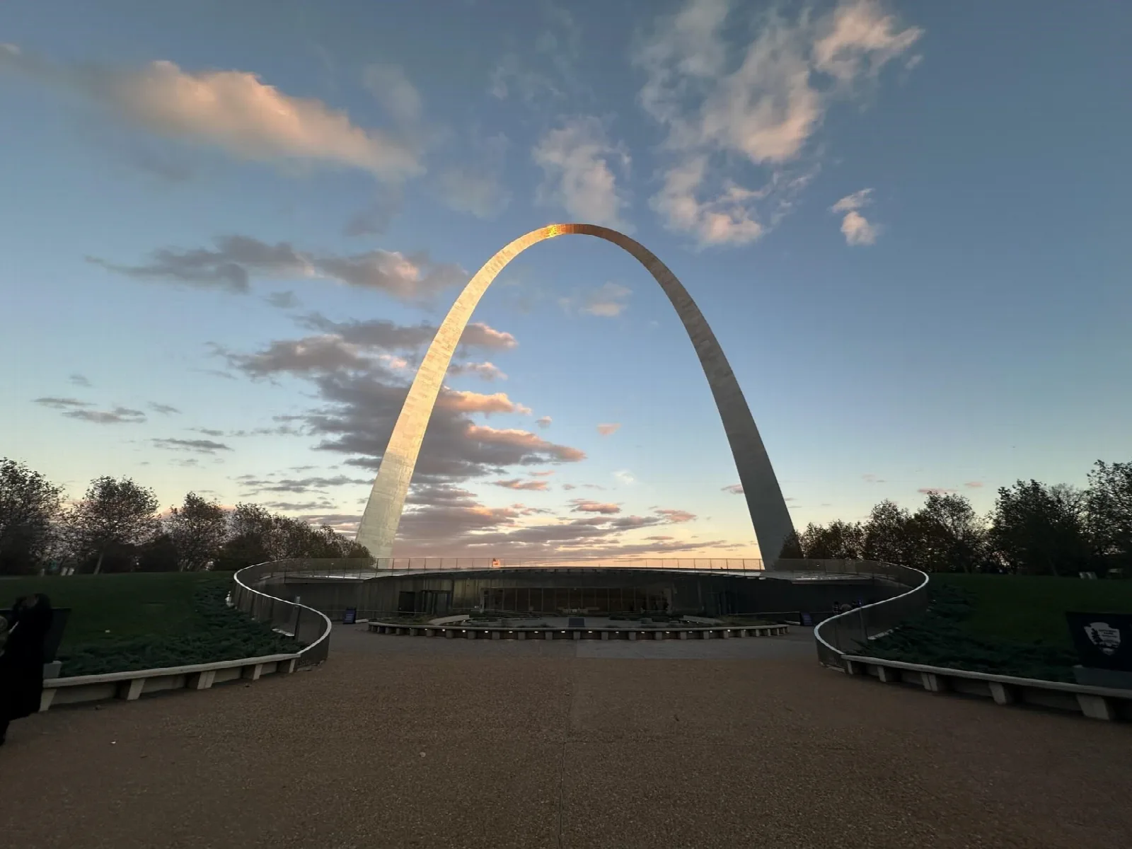 The stainless steel arch catching warm light beneath a sky of scattered clouds