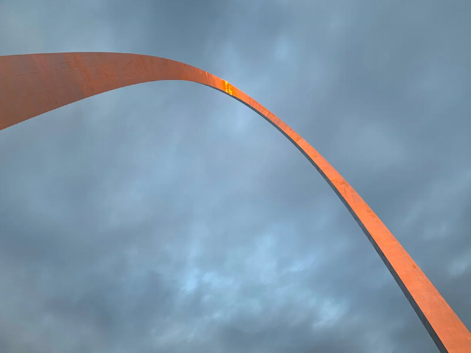 Looking up at the curve of the arch glowing orange against gray clouds