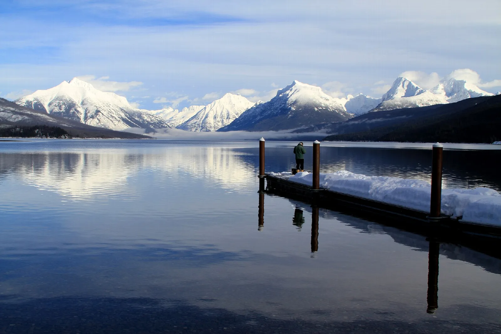Snowy peaks reflected in a calm lake beside a wooden dock
