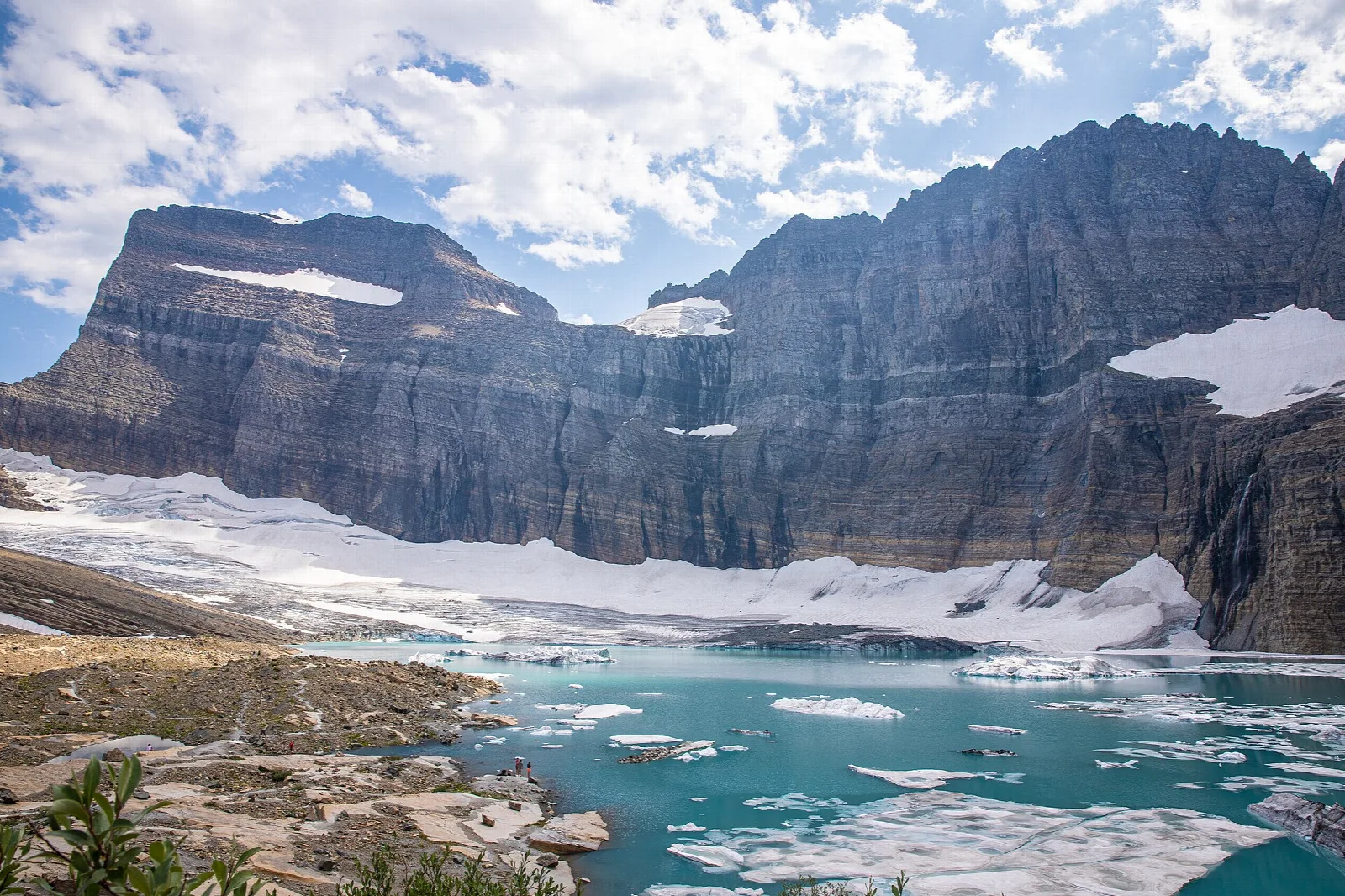 A glacier and floating ice in a milky turquoise lake below towering layered rock walls