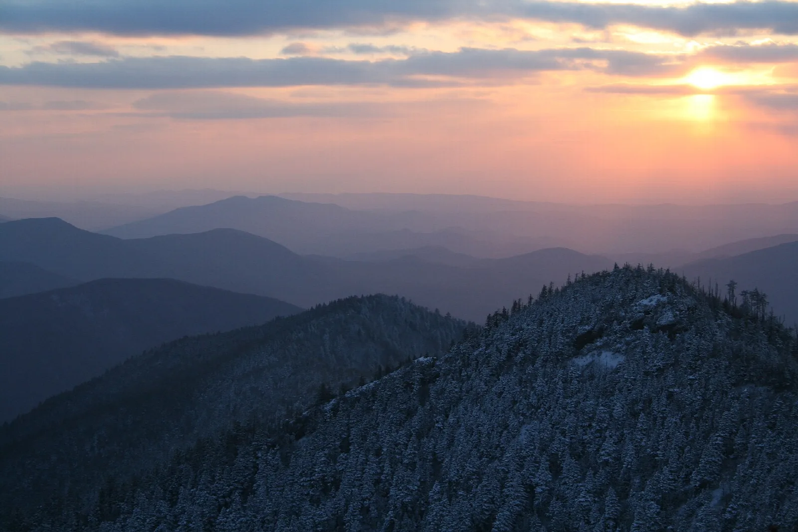 Layers of blue mountain ridges fading toward a setting sun