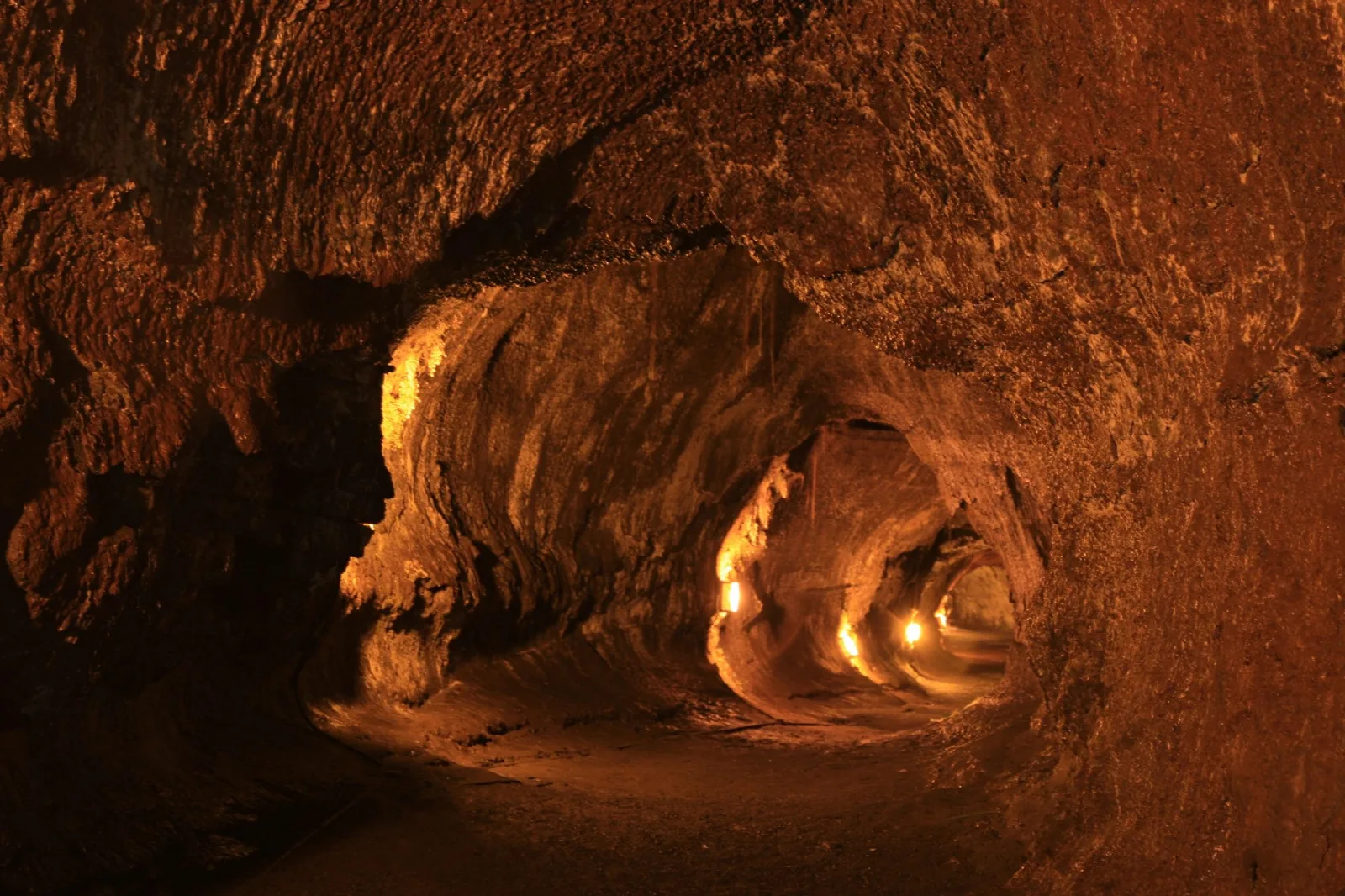 A lit tunnel of smooth lava rock curving into darkness