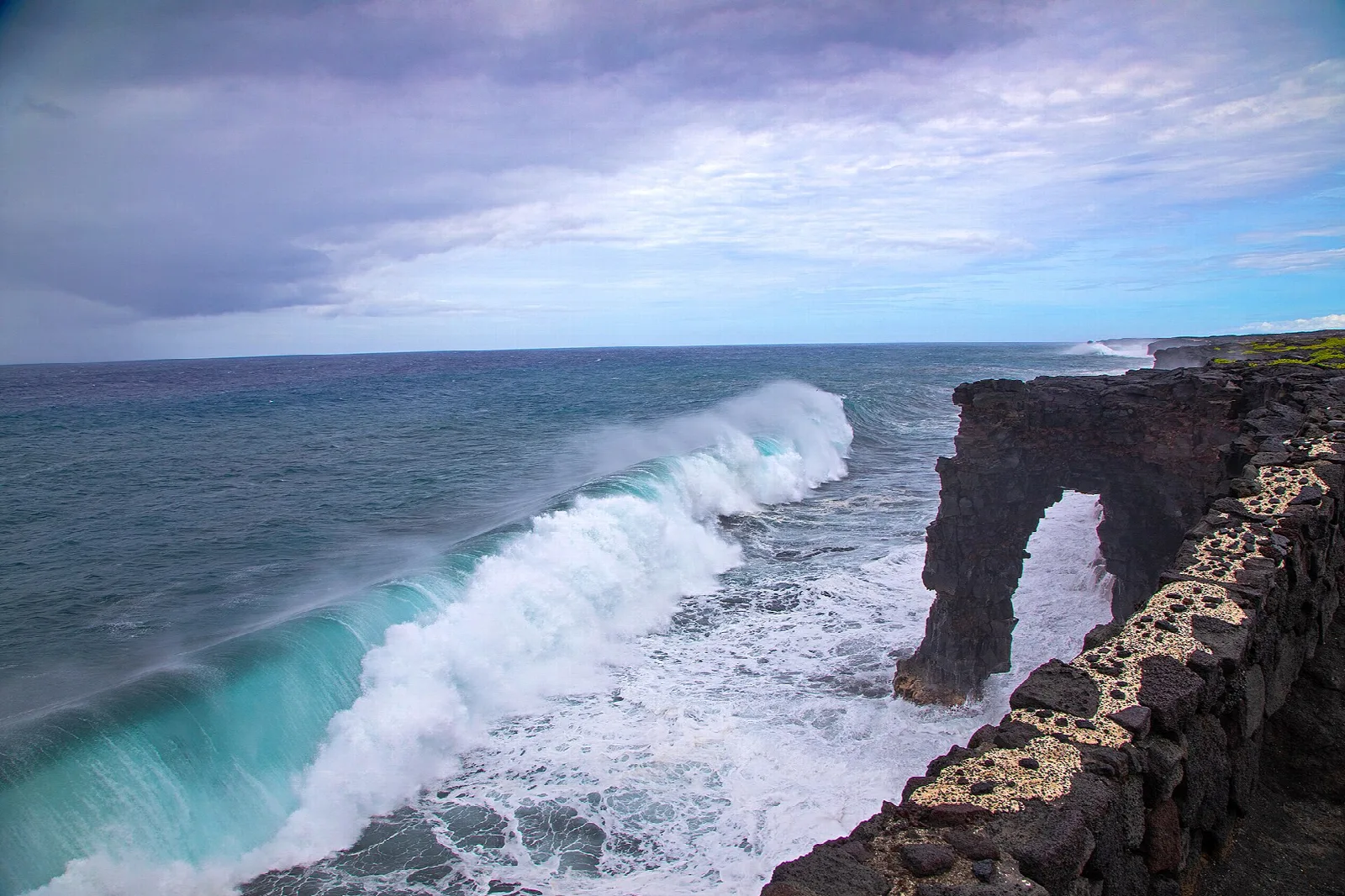 Big surf breaking against a natural lava-rock arch on a sea cliff
