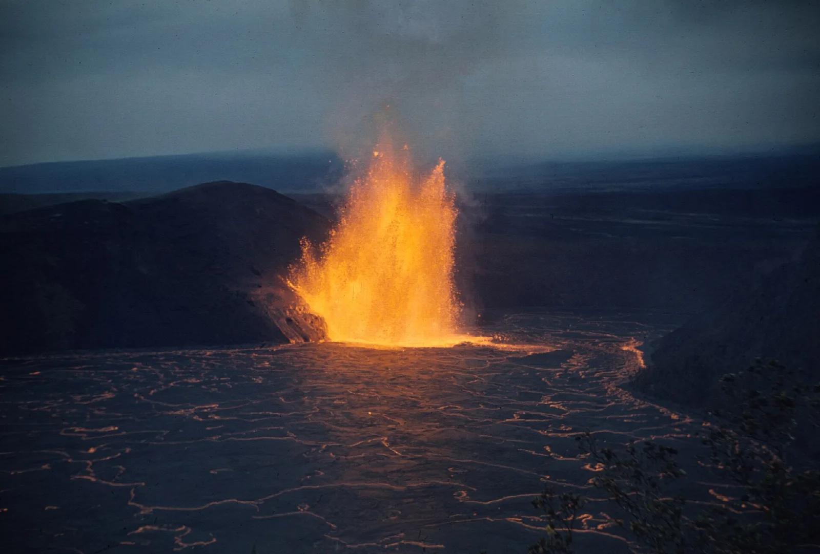 A glowing lava fountain reflected across a lava lake in Kīlauea Iki crater at dusk, 1959