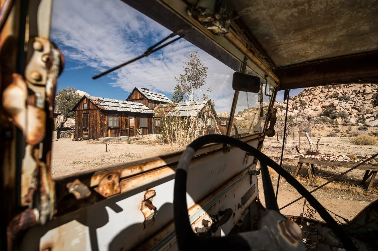 an historic wood house seen through the missing windshield of an old, rusty vehicle