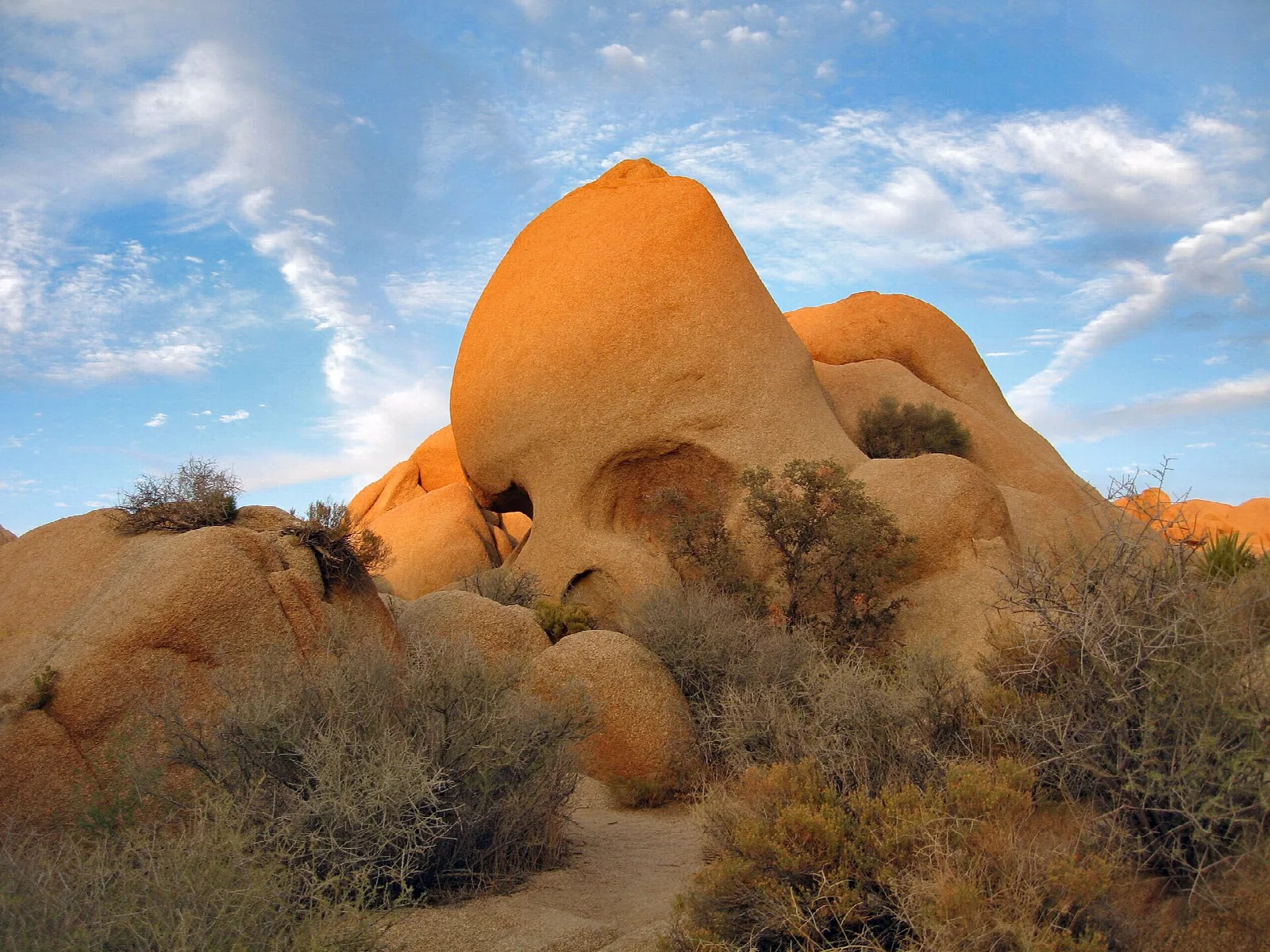 A rounded granite boulder with two eye-like hollows, glowing orange in late light