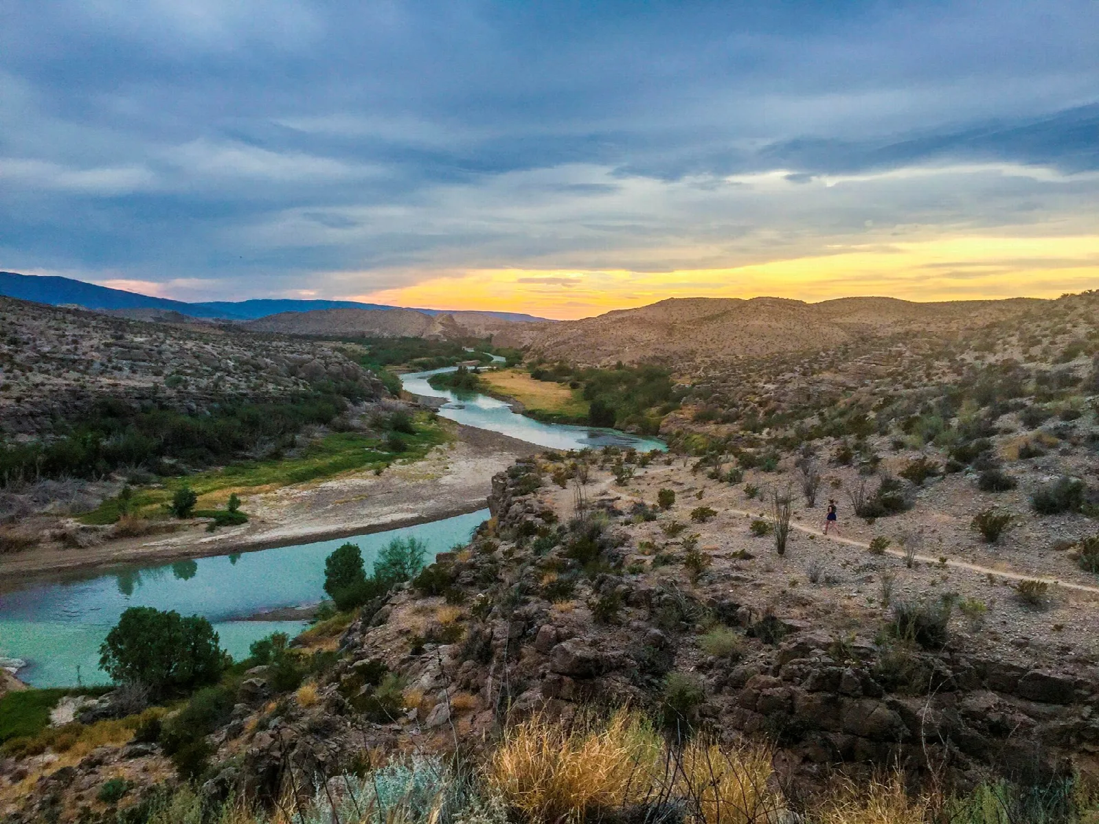 The Rio Grande winding through desert hills under a golden sunset sky