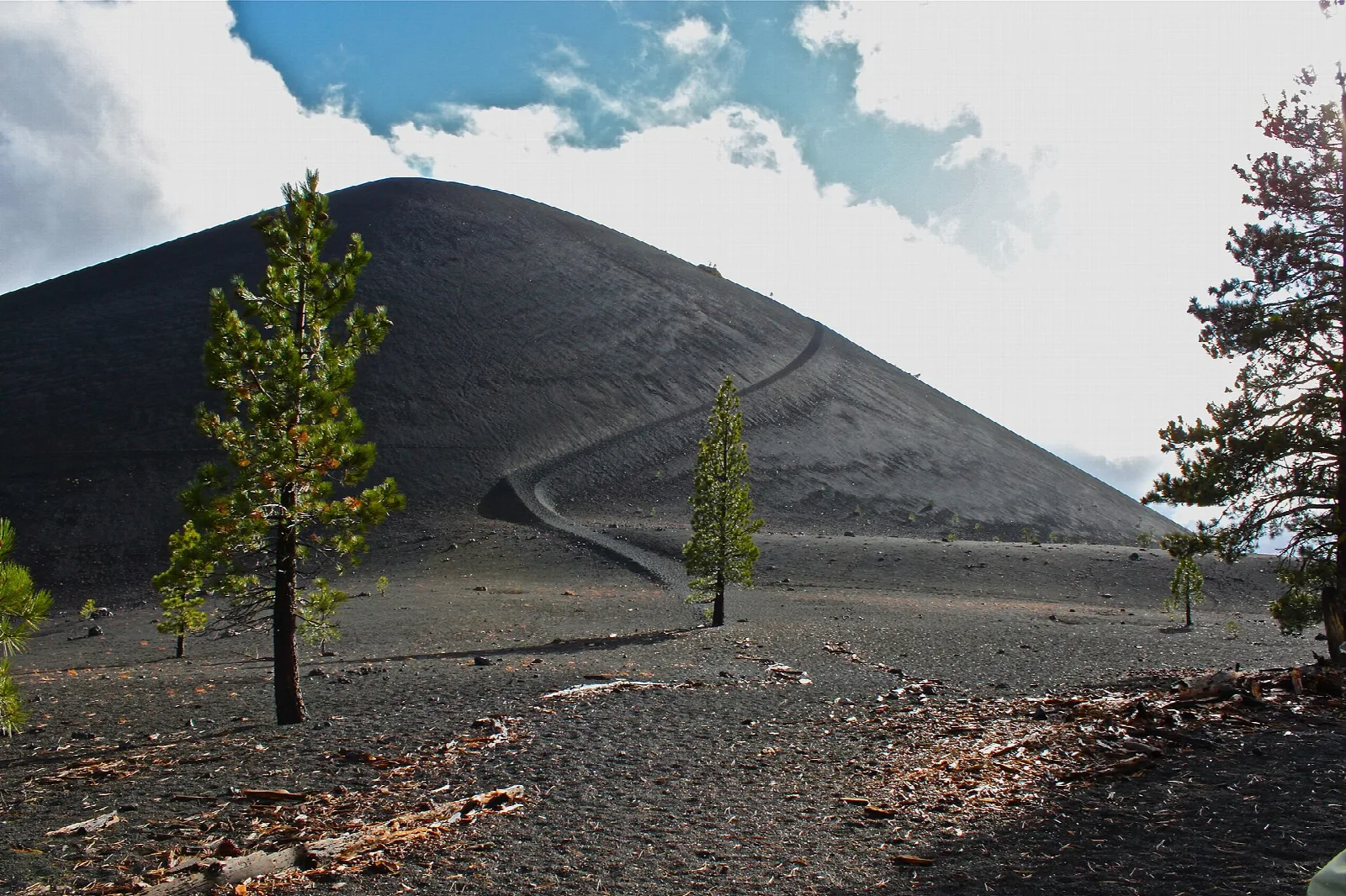 A dark, symmetrical cinder cone with a trail climbing its side