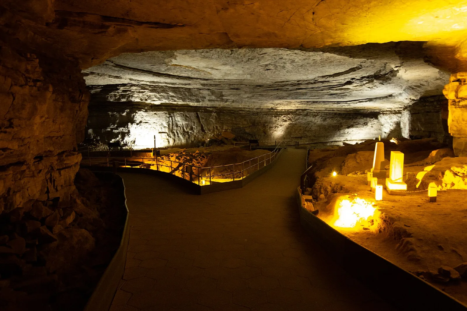 A vast cave room with a broad, flat ceiling, lit along its walkway