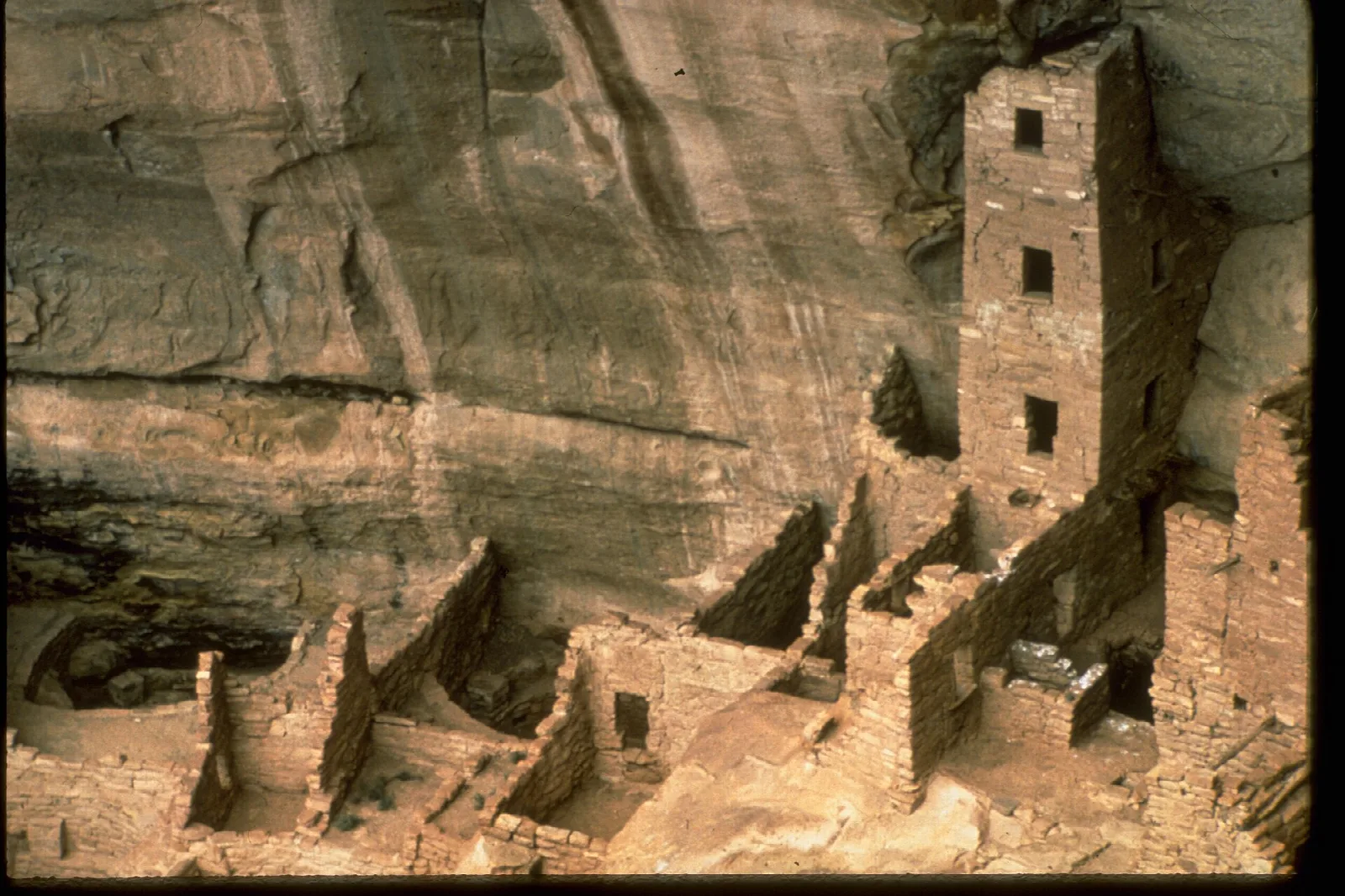 A tall stone tower and ruined rooms in a sandstone alcove