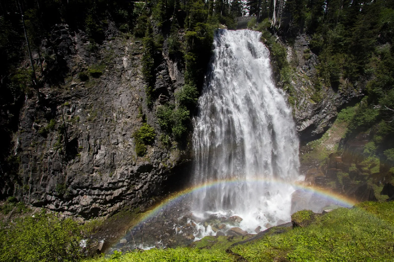 A waterfall pouring over a dark cliff with a rainbow in its spray