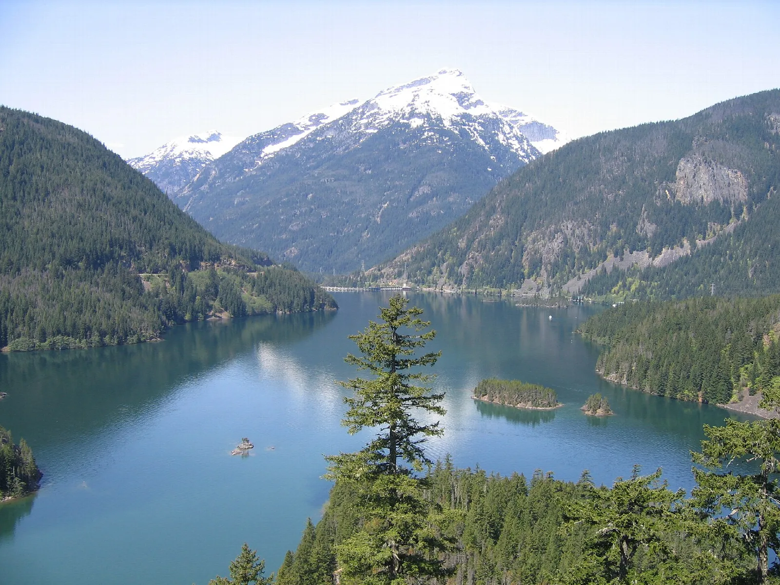 A turquoise glacial lake between forested mountains below a snowy peak, in the park complex's Ross Lake National Recreation Area