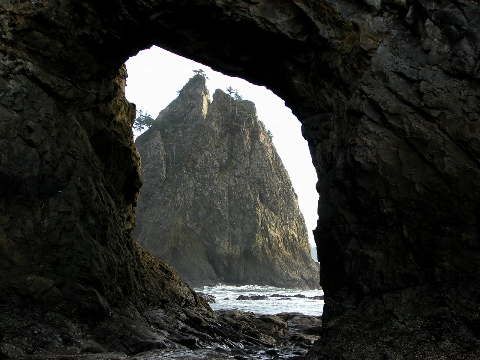 A sea stack framed through a natural rock arch on the coast