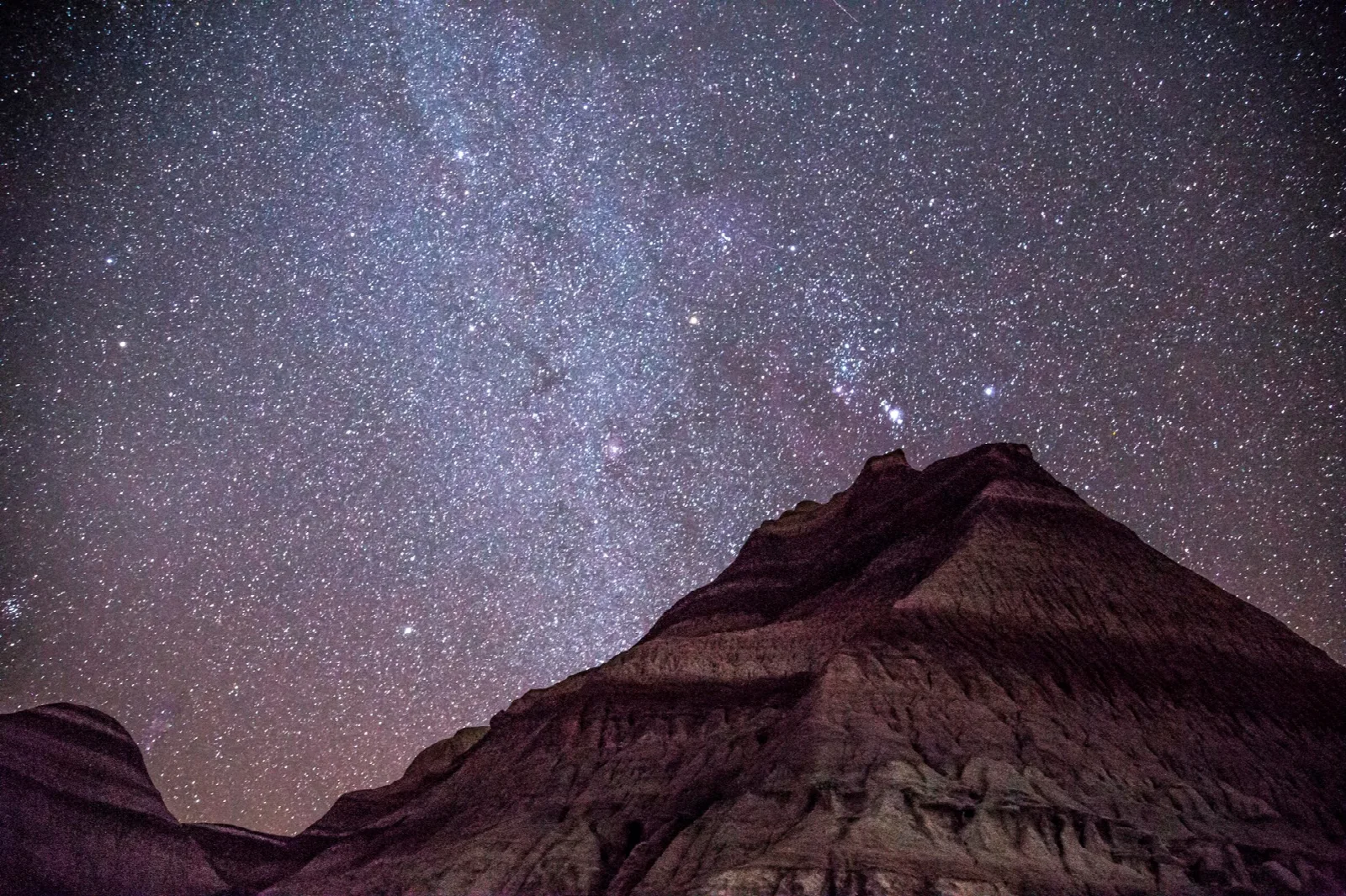 The Milky Way above a dark, layered badlands hill