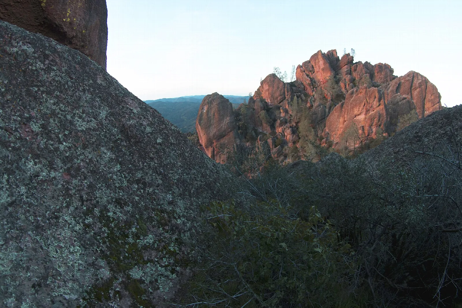 Red-lit pinnacle formations seen past a dark boulder at dusk