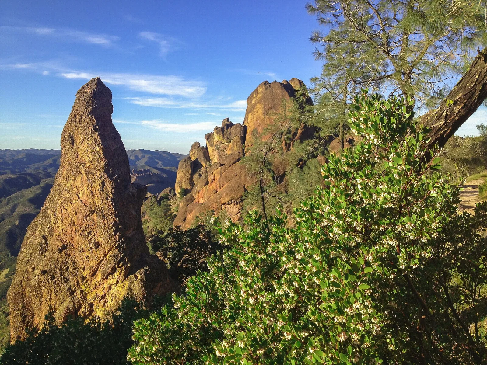 A tall rock spire and craggy pinnacles lit gold above green chaparral