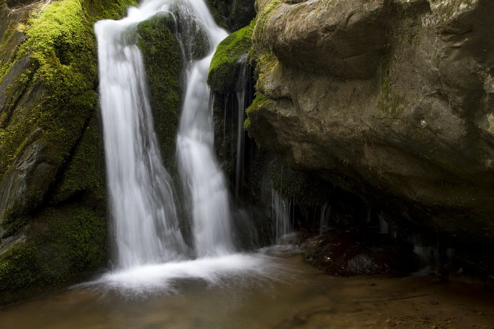 A waterfall pouring over mossy rock ledges in a shaded ravine