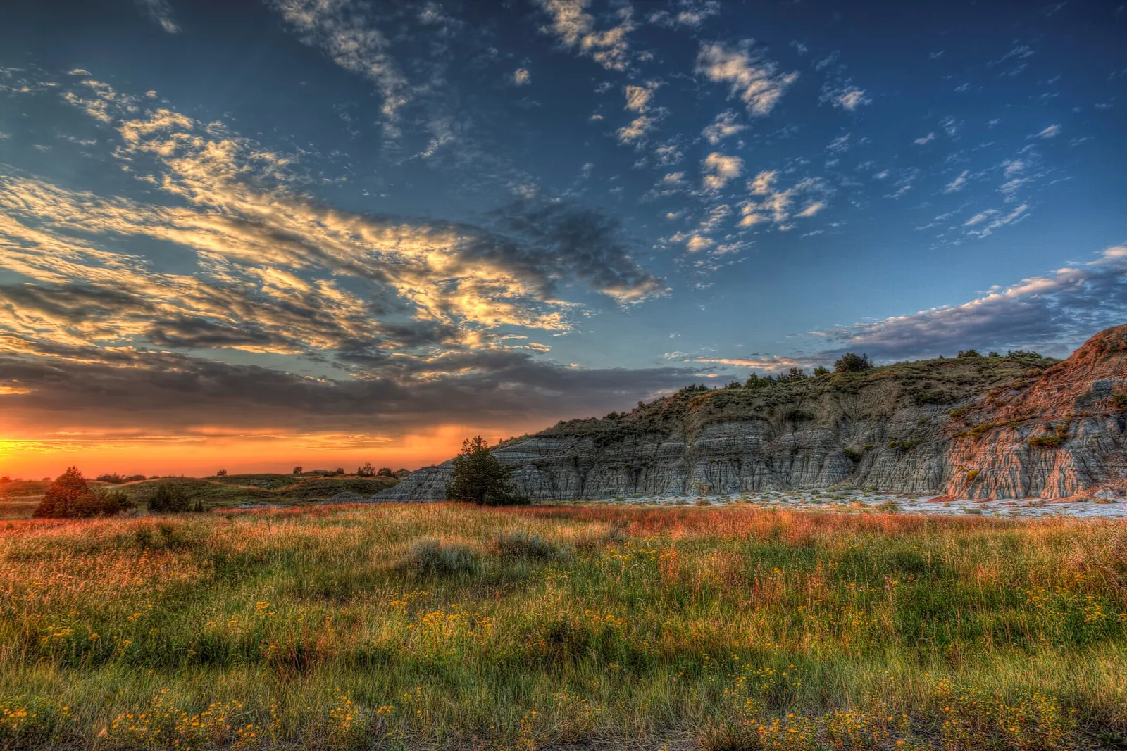 A vivid sunset sky over golden grassland and a long badlands ridge