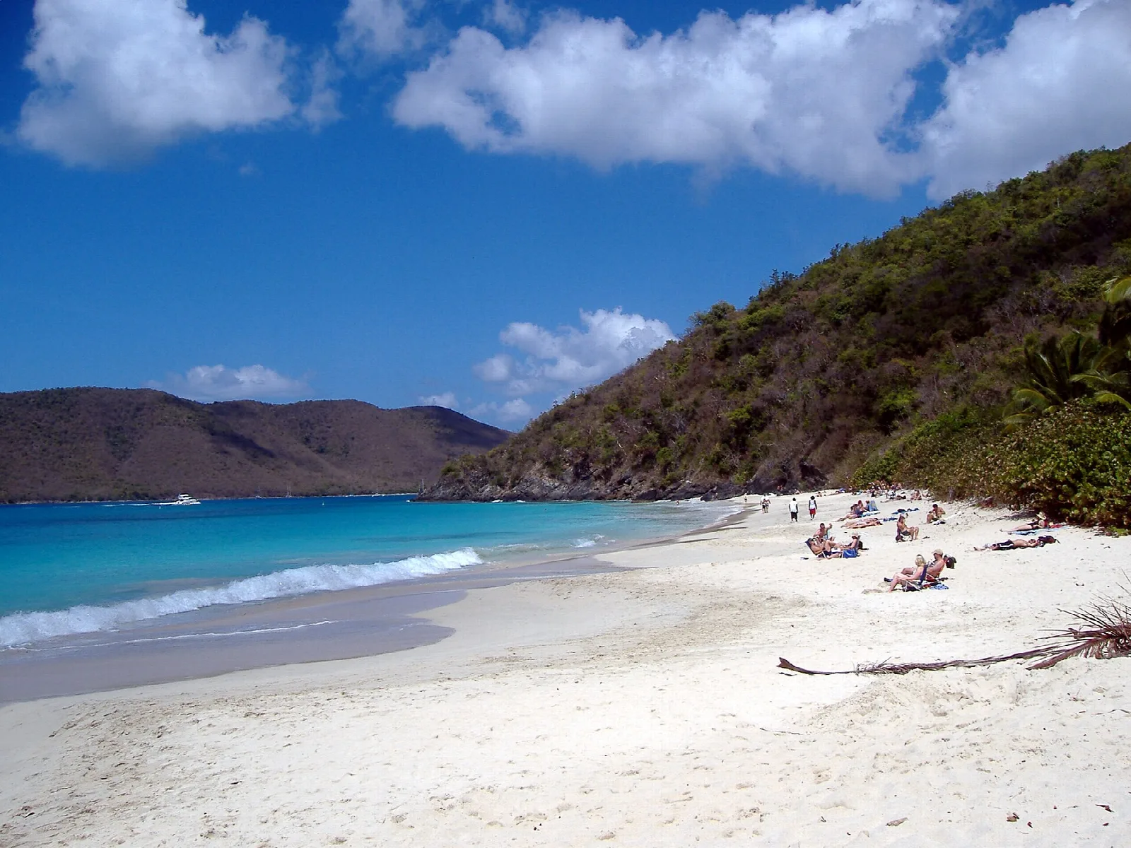 A white sand beach along clear turquoise water beneath steep green hills