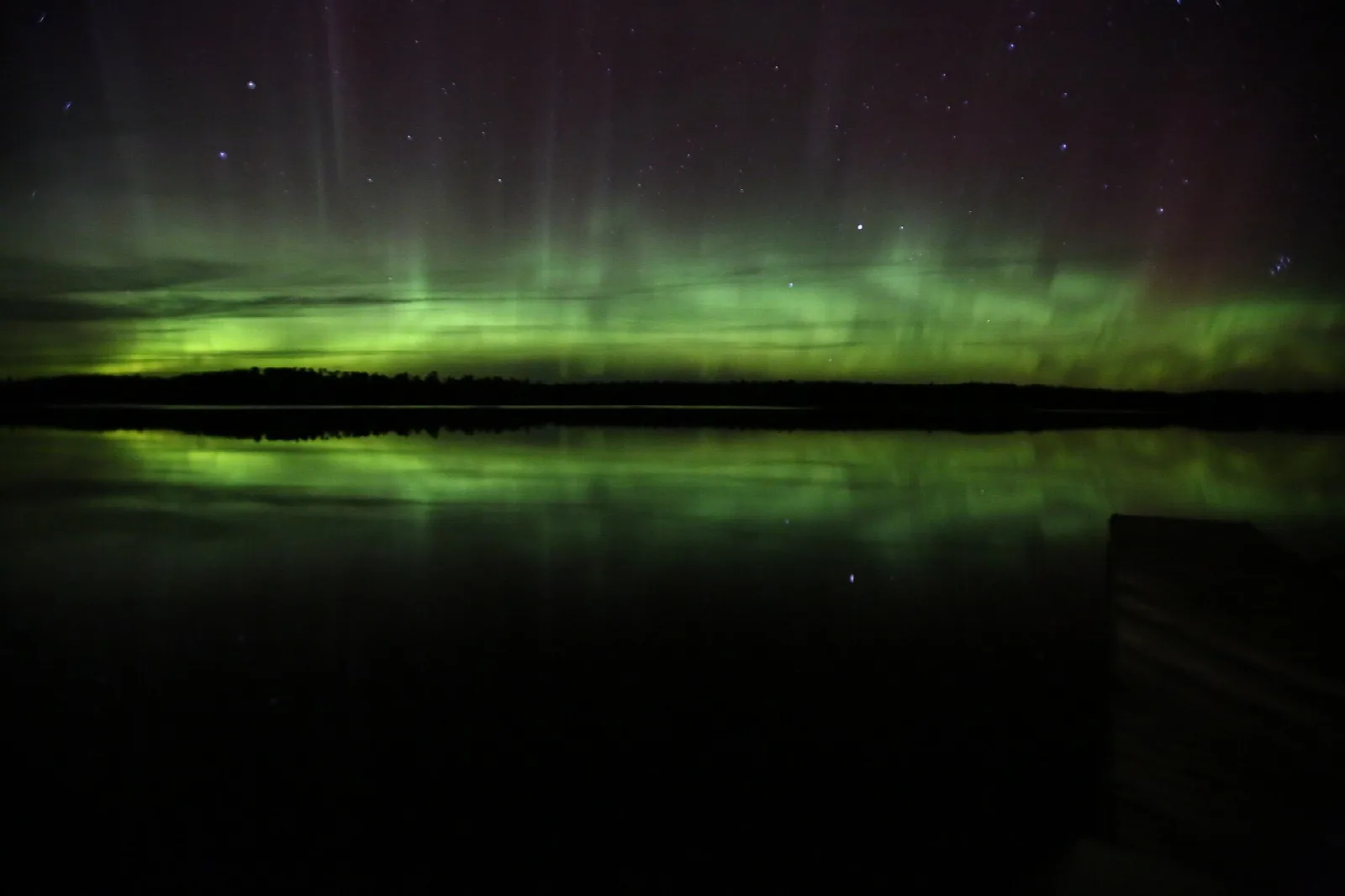 Green northern lights glowing over a calm lake that mirrors them