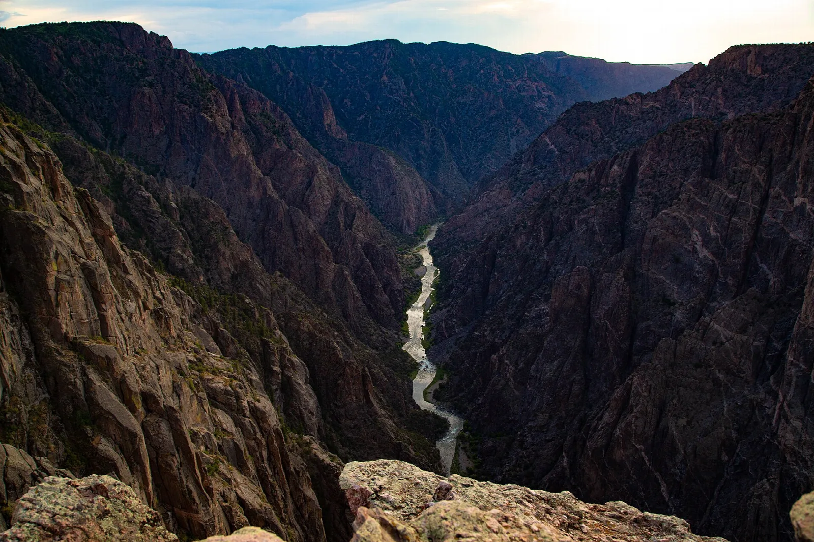 Looking down a deep, narrow canyon to a glint of river far below at sunset
