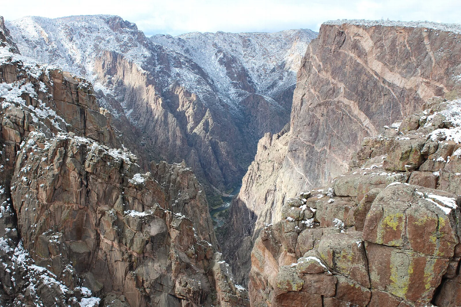 Snow dusting the rims and ledges of a deep canyon with a veined rock wall