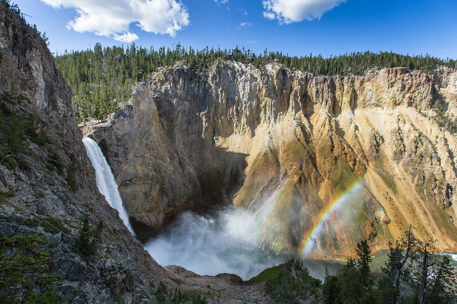 A waterfall plunging into a yellow canyon with a rainbow in its spray