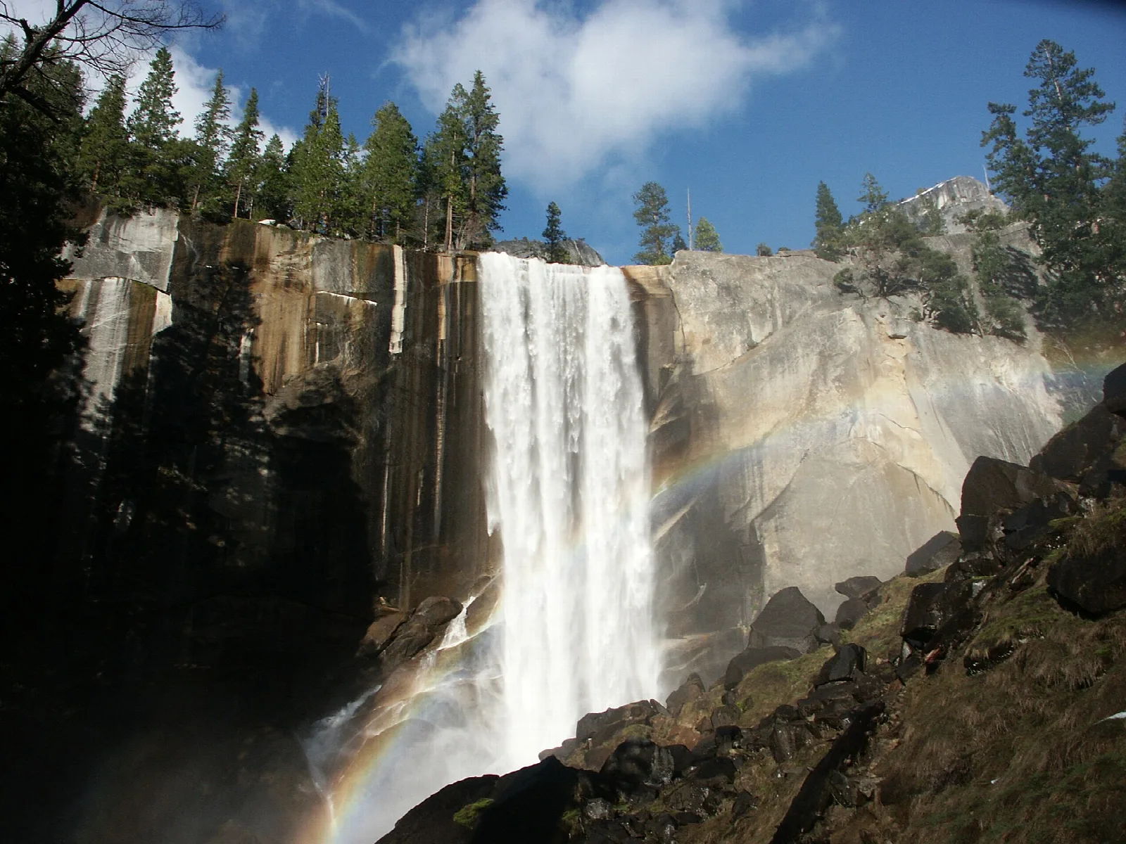 A broad waterfall pouring over a granite cliff with a rainbow in the mist