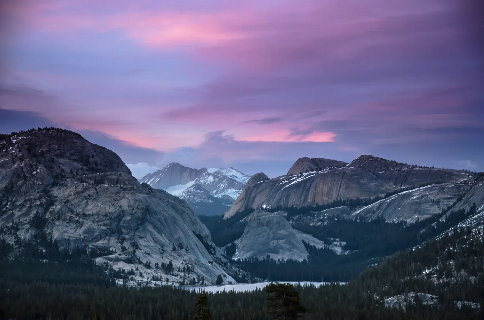 Granite domes around a lake under a pink and purple sunset sky