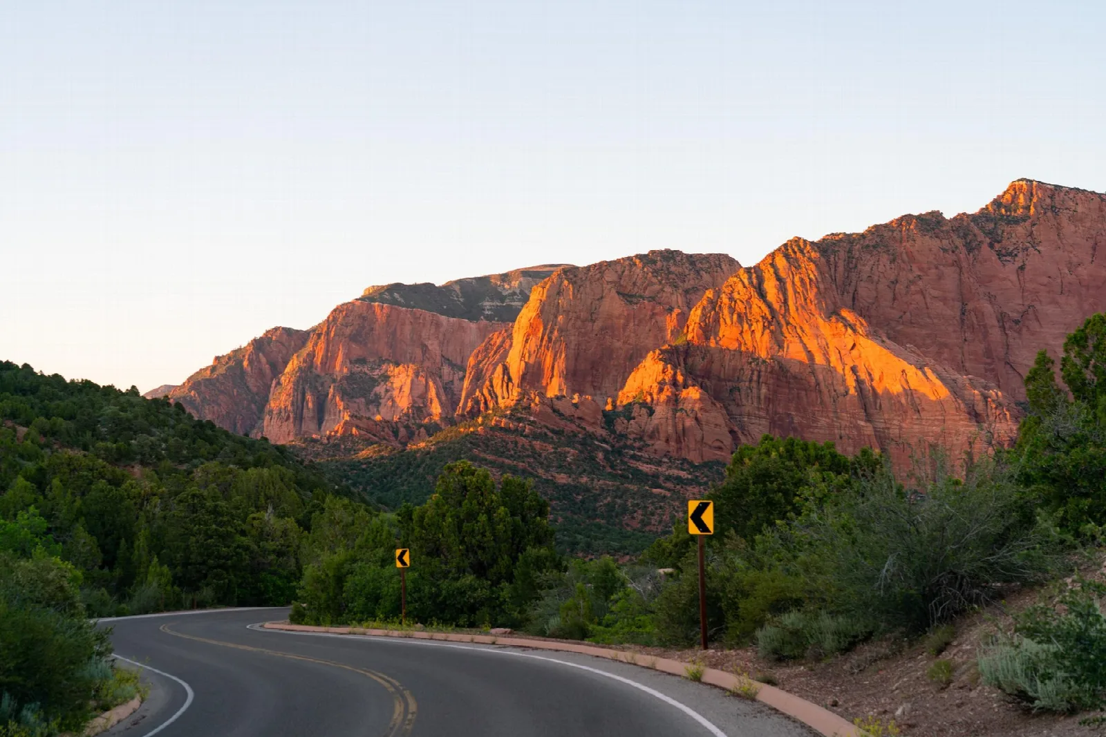 A road winding below red cliffs lit by the setting sun