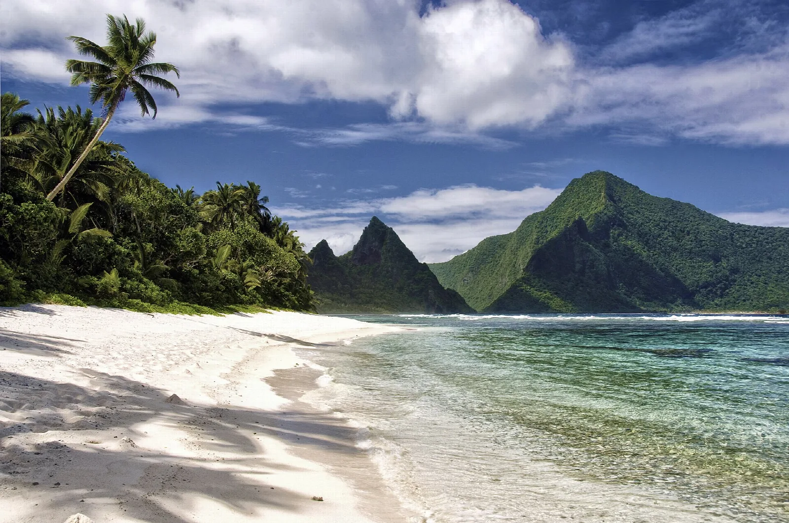 A white sand beach and clear lagoon below steep, jungle-covered peaks