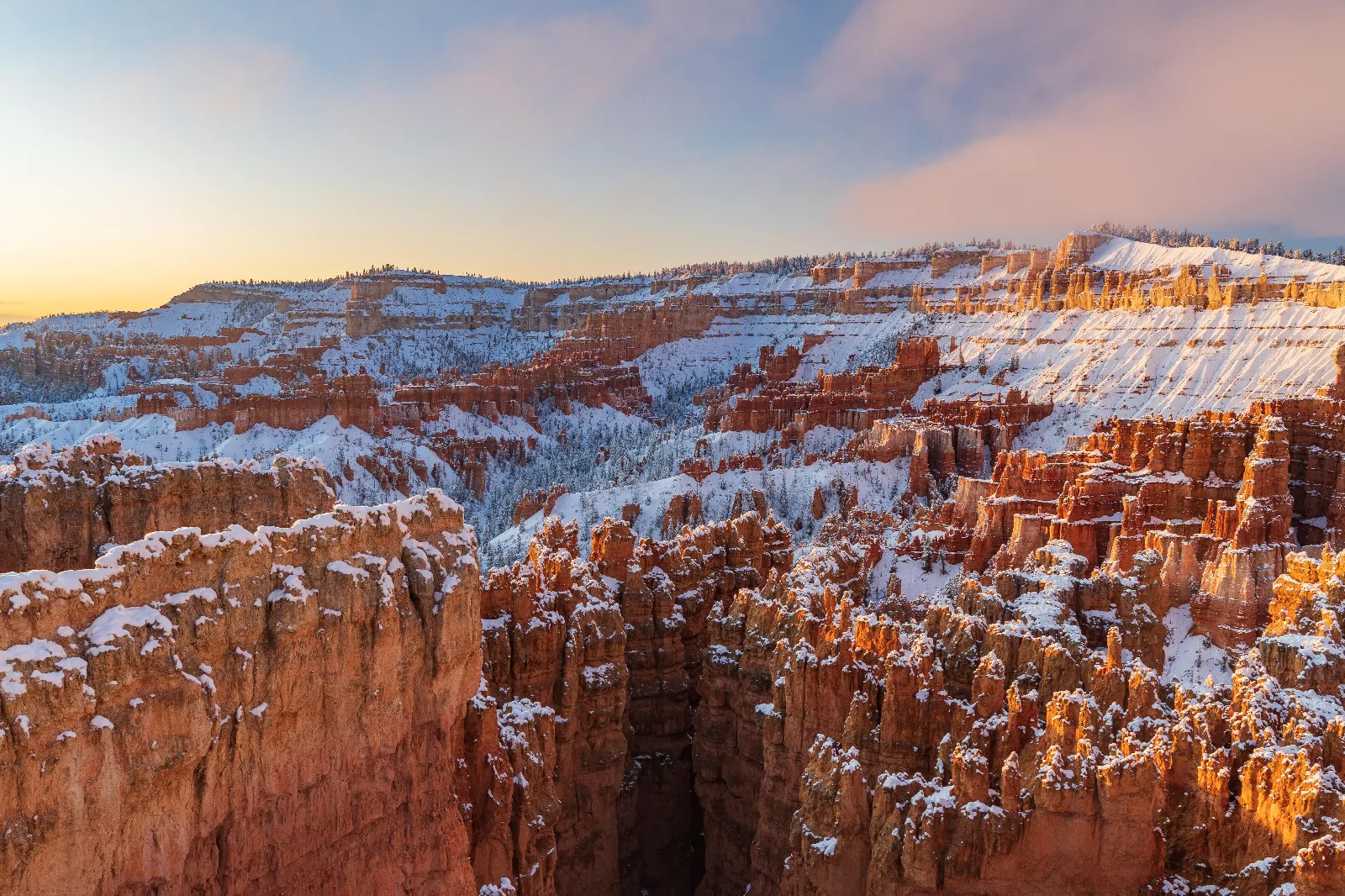 Snow blankets a red rock landscape of tall rock spires beneath an early morning sky