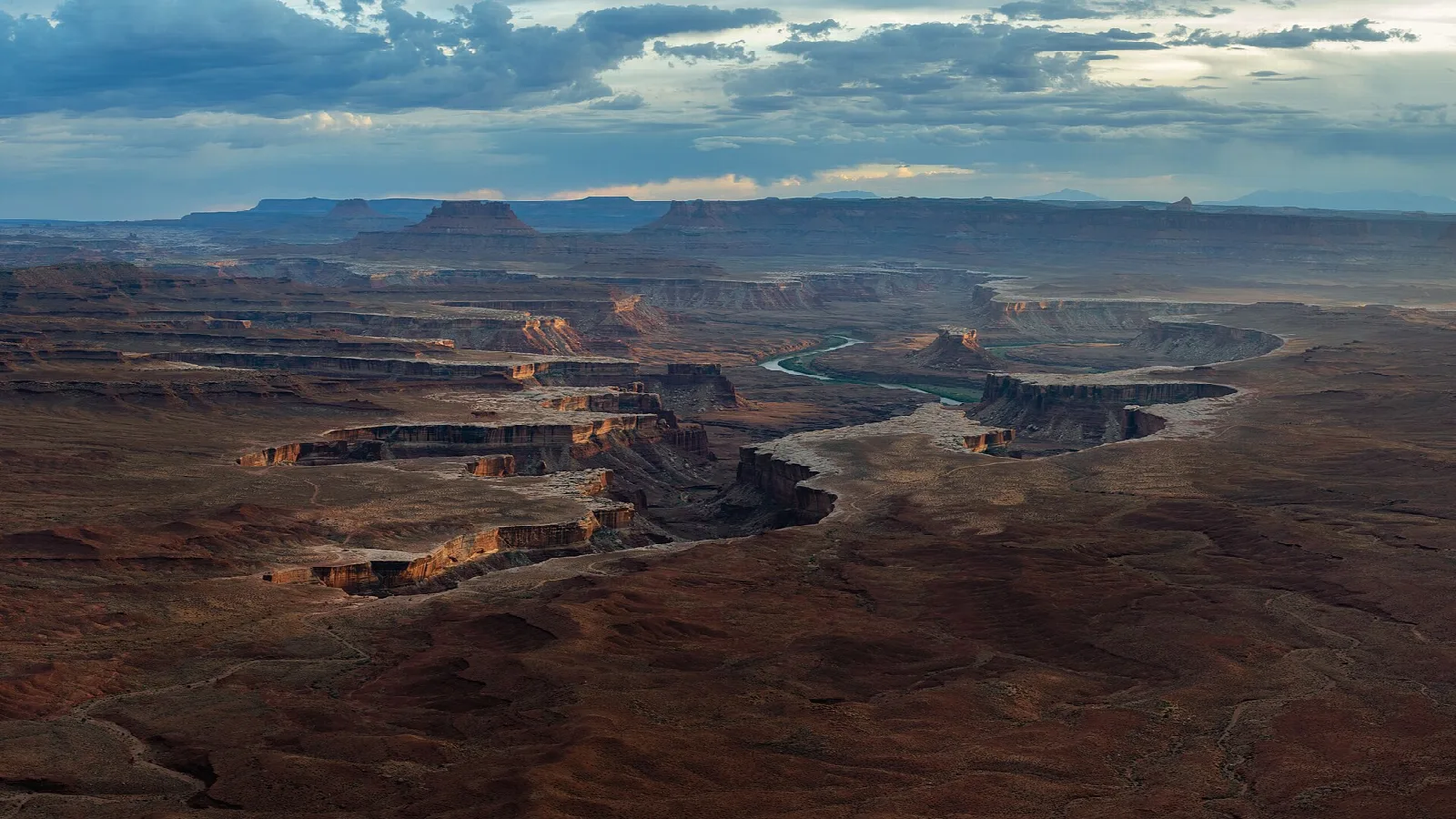 A vast maze of canyons and mesas under dramatic clouds, the Green River winding below