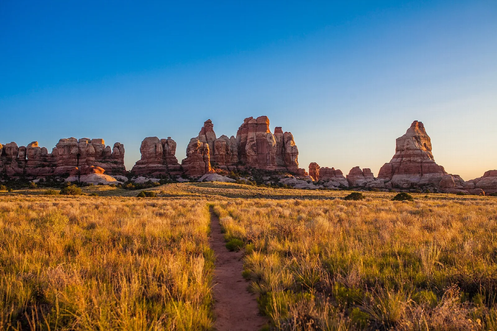 A trail through golden grassland toward banded sandstone pinnacles at dusk