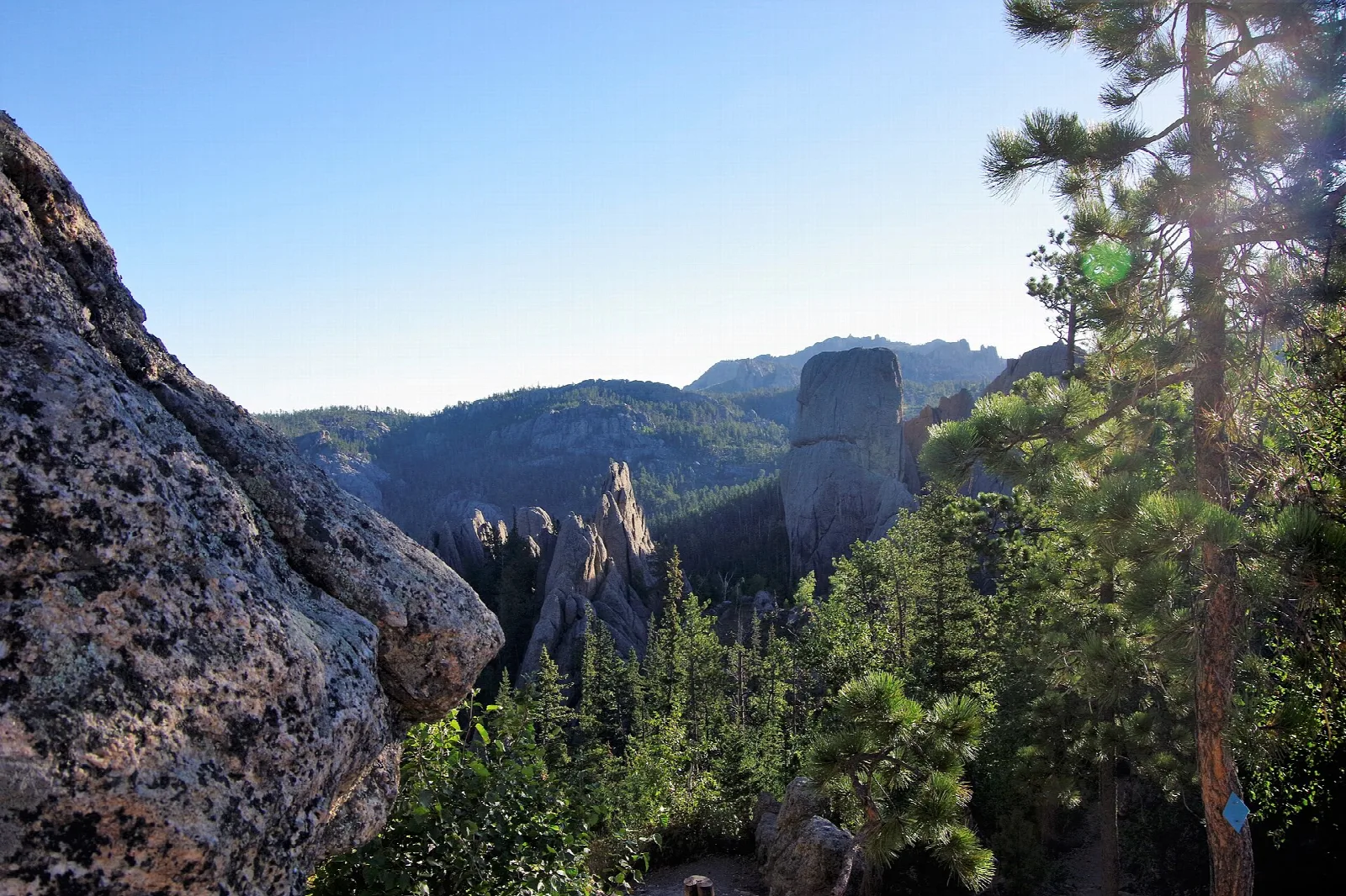 View over forested hills and a tall rock needle from a pine-lined overlook