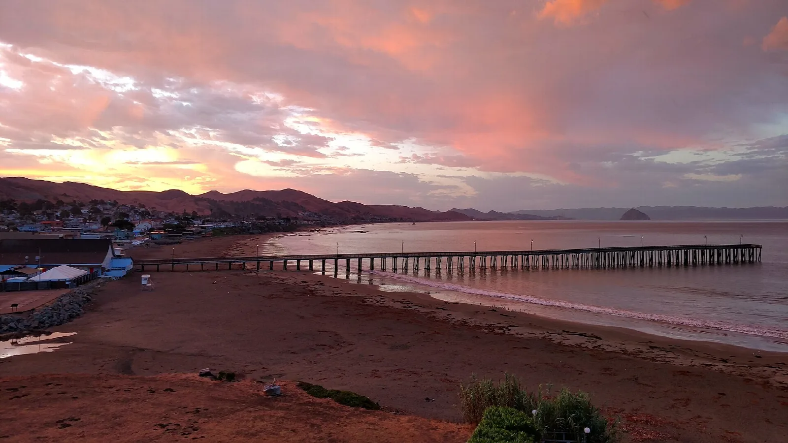 Long pier stretching into the ocean under a pink sunrise sky