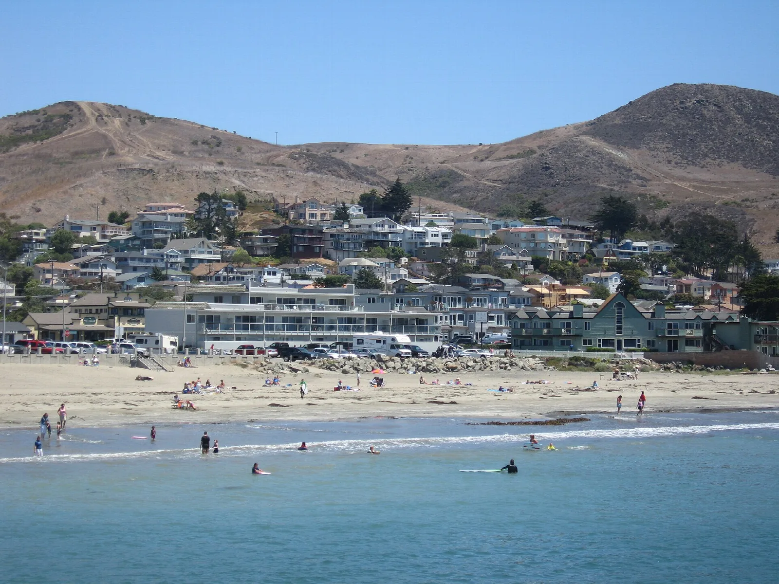Sandy beach with swimmers and hillside homes behind
