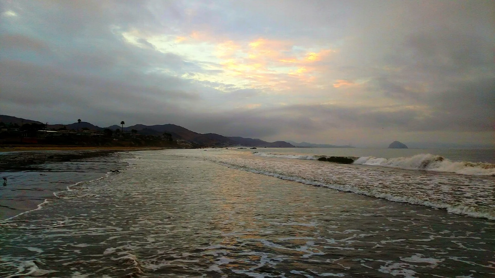 Wet sand and waves at sunrise with distant hills