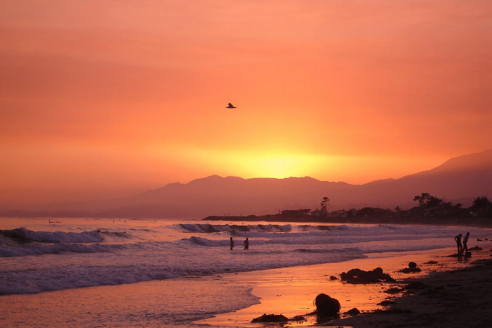 Orange sunset over surf and a beach with distant mountains